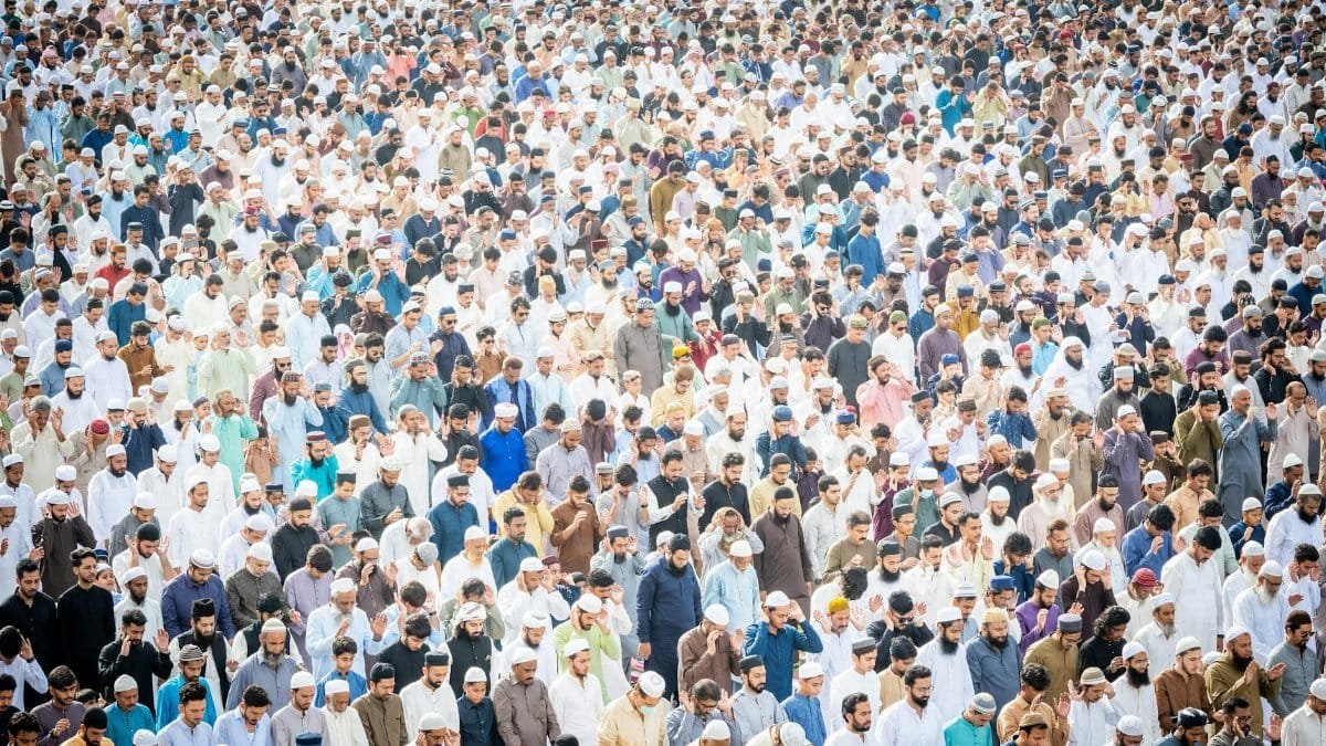 Aerial view of a large group of men gathered outdoors for prayer during a religious ceremony.