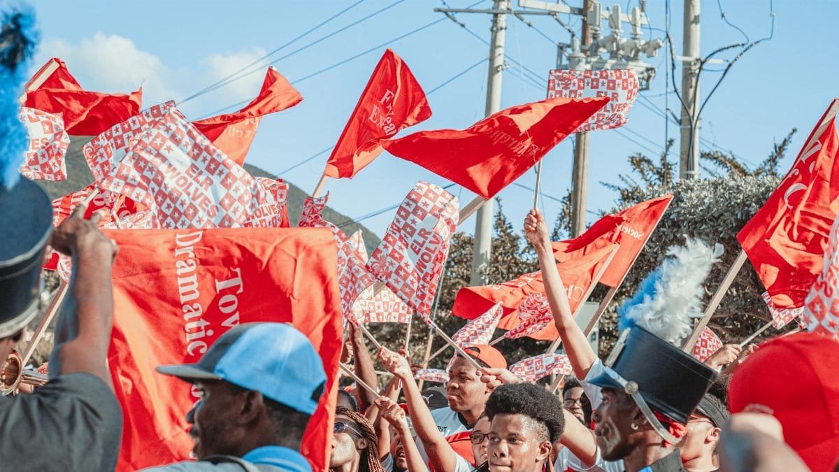Colorful street parade with people waving red flags, celebrating outdoors.