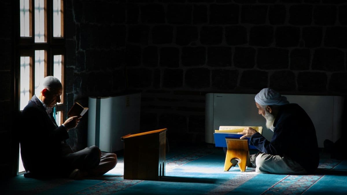 Two men engaged in deep religious study in a dimly lit mosque in Diyarbakır, Türkiye.