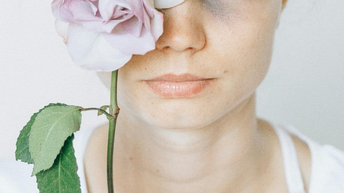 A conceptual close-up of a caucasian woman holding a flower, symbolizing pain and beauty.