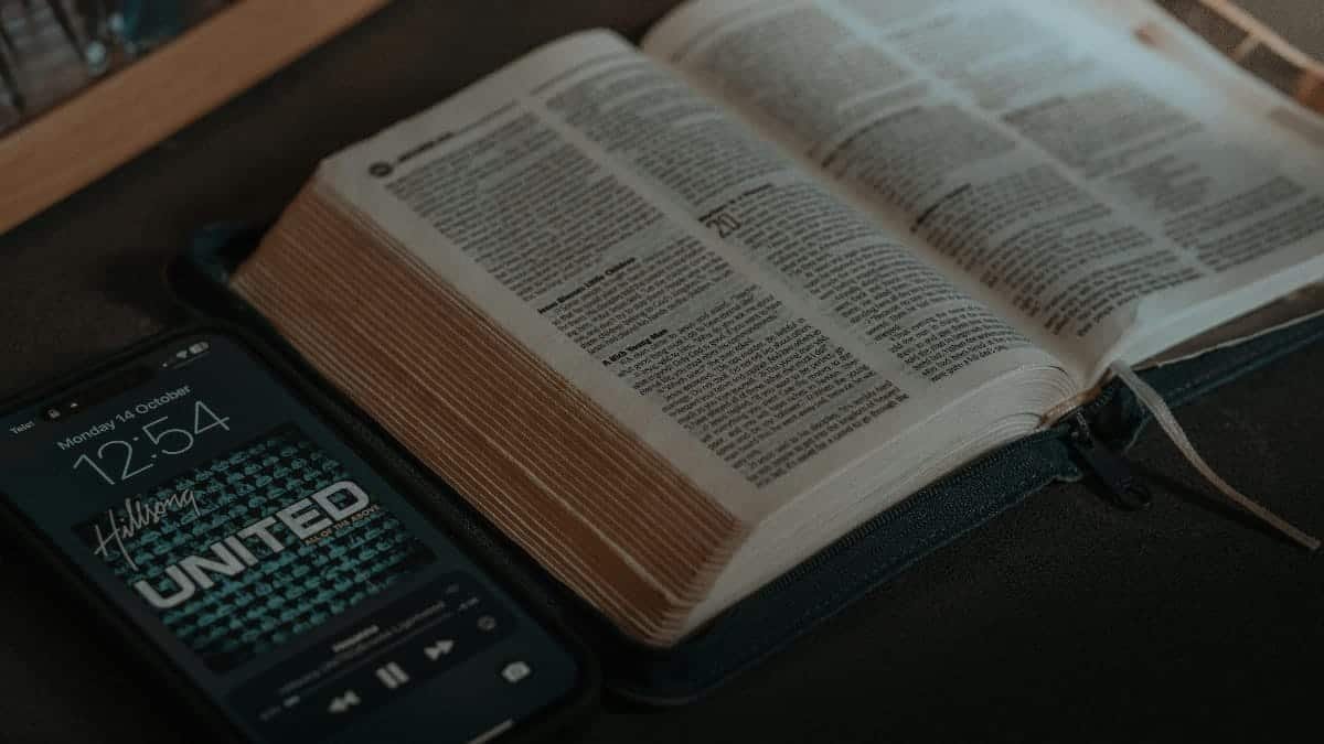 Open Bible on a table next to a smartphone displaying a playlist, conveying a spiritual and modern theme.
