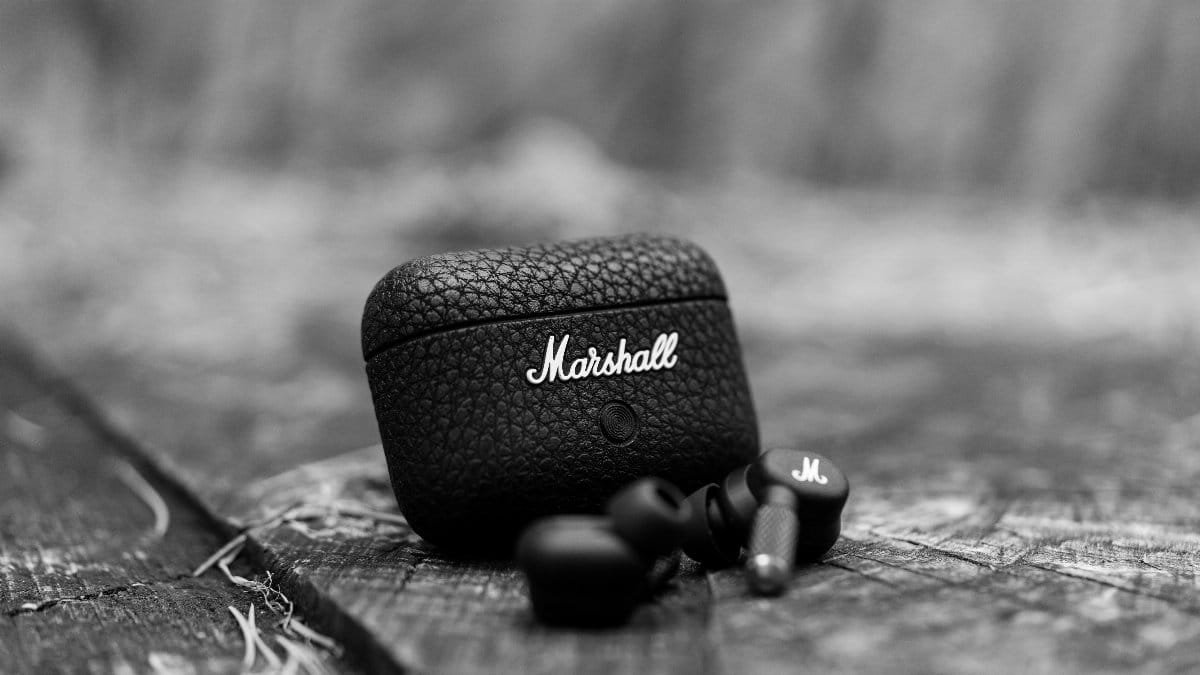 Black Marshall earbuds resting on textured wood. Close-up shot highlighting design and texture.