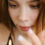 A woman in a black tank top gazes thoughtfully at a lit candle indoors. via Pexels
