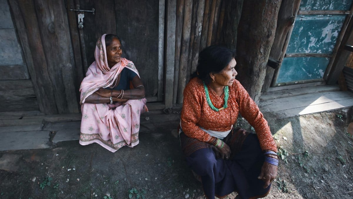 Two women sitting outdoors in a traditional rural setting, embracing cultural heritage.