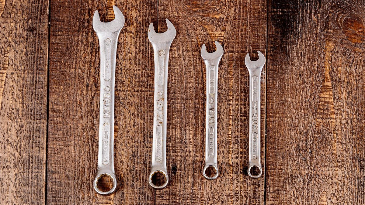 Flat lay of four metal wrenches on a rustic wooden surface, ideal for workshop or DIY themes.