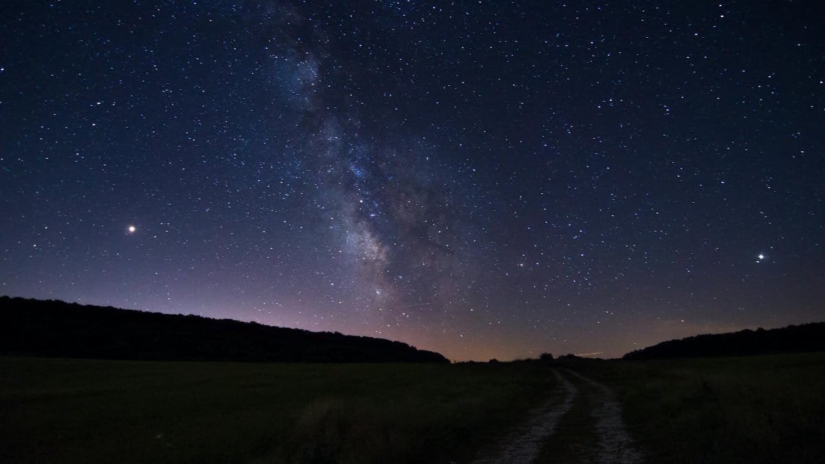 A stunning view of the Milky Way dominating the night sky over a serene open field pathway.