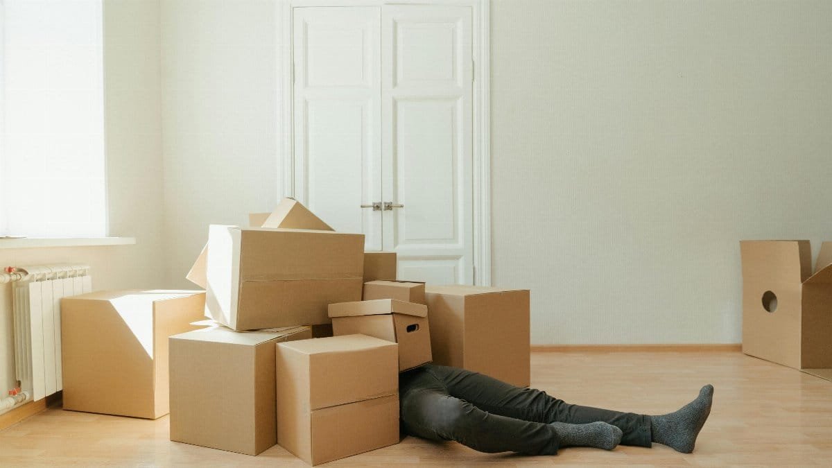 Person on floor surrounded by cardboard boxes during moving; concept of stress and relocation.