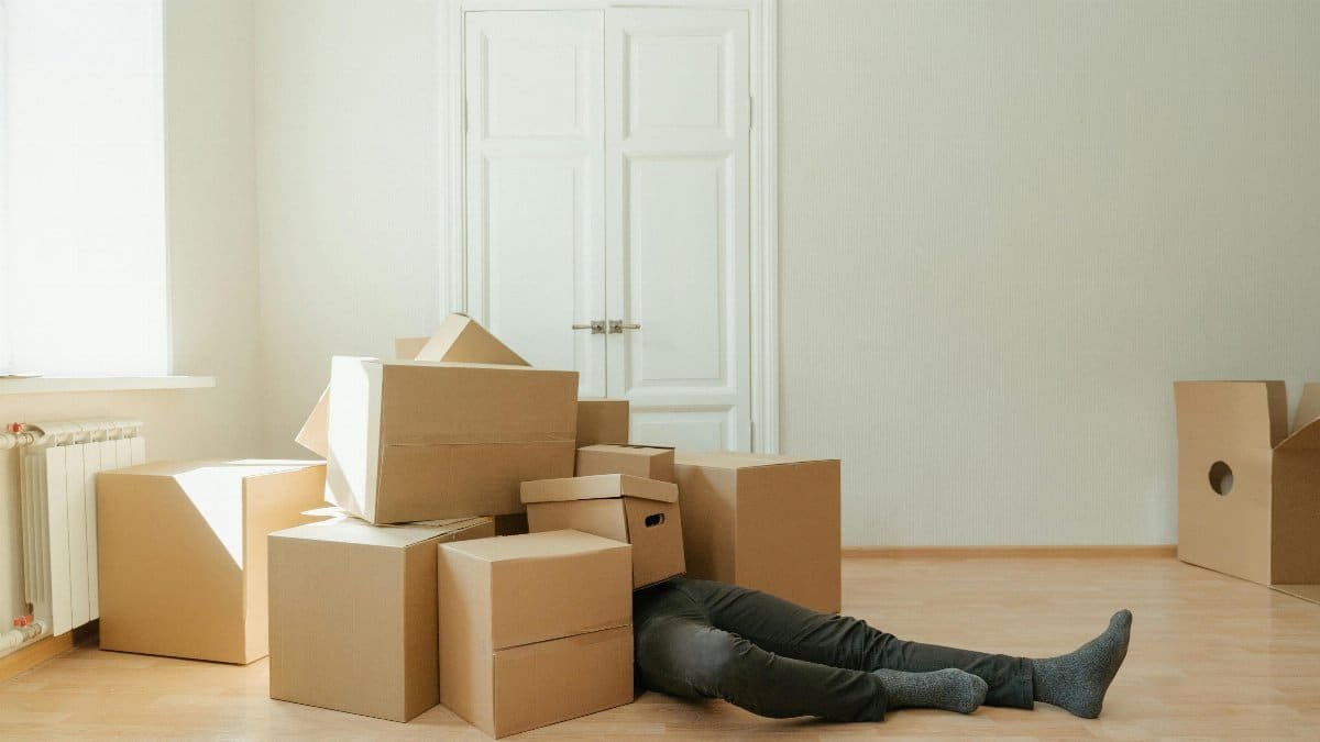Person on floor surrounded by cardboard boxes during moving; concept of stress and relocation.