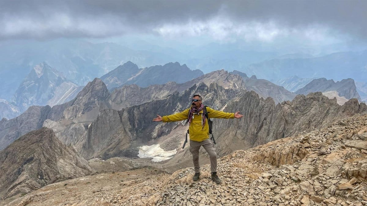 A man in a yellow jacket enjoying the breathtaking view from a mountain summit.