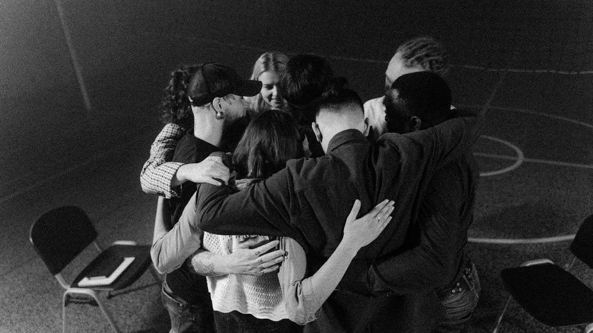A diverse group in a supportive embrace during a meeting, symbolizing unity and connection.