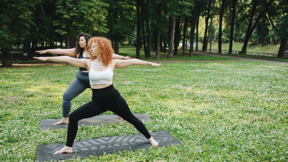 Two women practicing yoga in a serene outdoor park setting, enhancing their physical and mental well-being.
