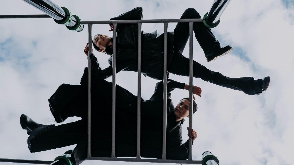 Two stylish women pose creatively on a playground structure against a dramatic sky.