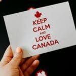 A card with 'Keep Calm and Love Canada' held against a dark background with maple leaf symbols.