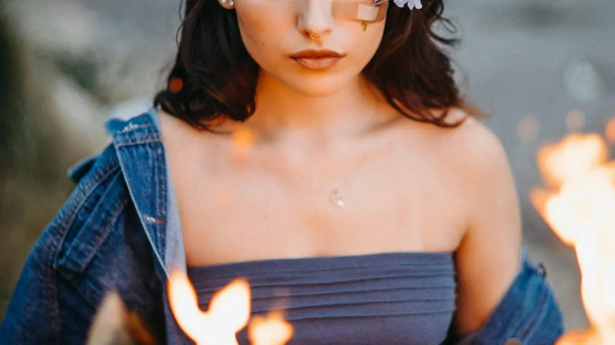 A woman with flowers on her face holds a burning newspaper, creating a dramatic scene.