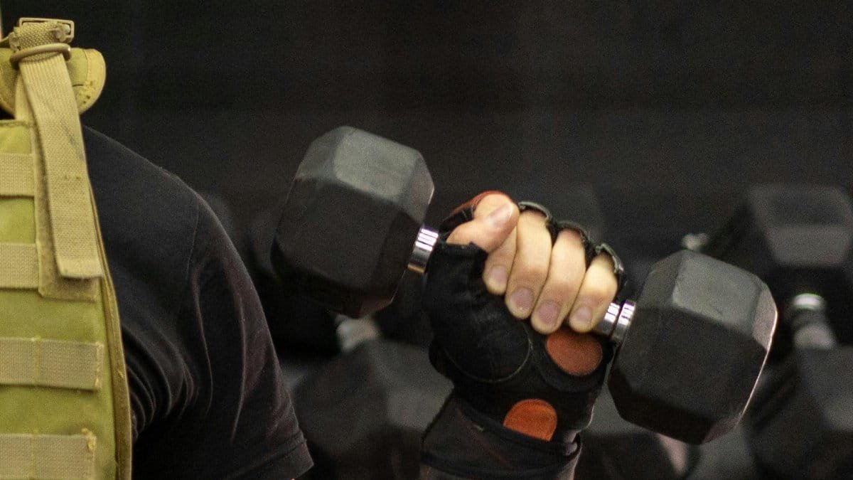 Side view of a person lifting a dumbbell while wearing a weighted vest in a gym.