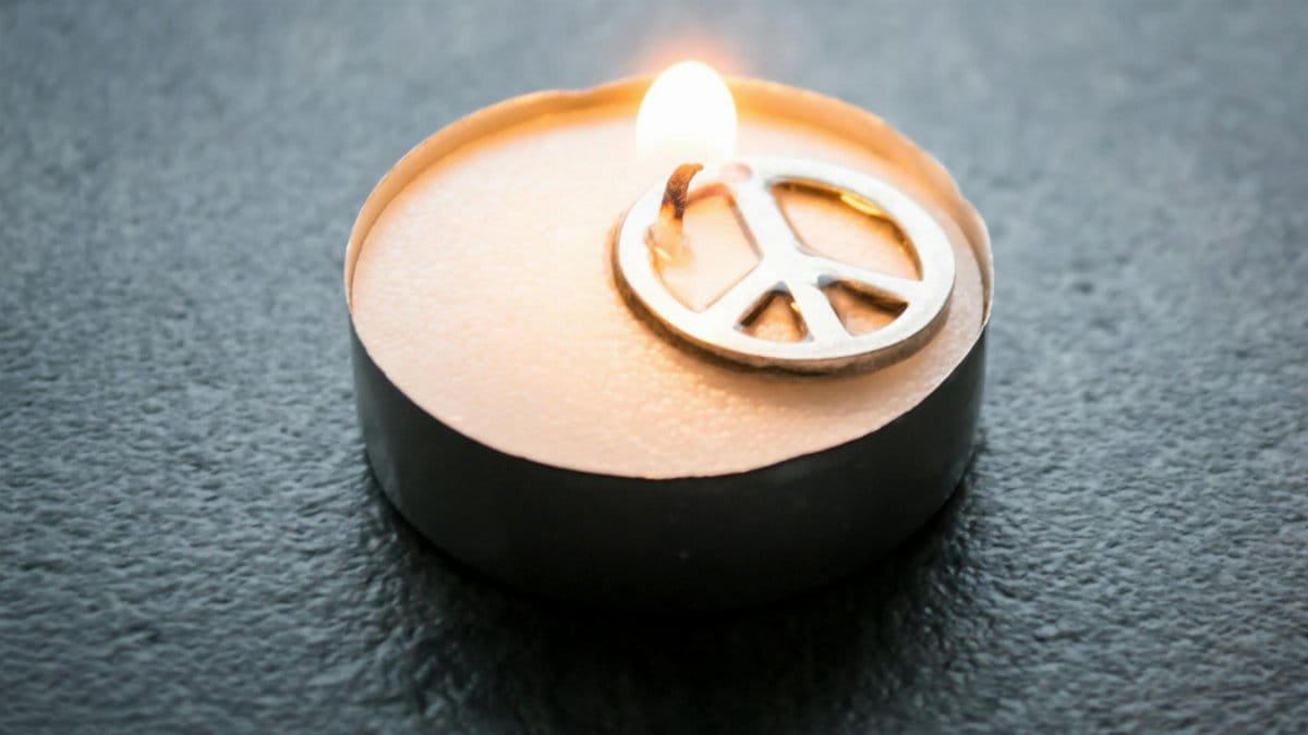 Close-up of a candle with a peace symbol, glowing warmly in the dark.