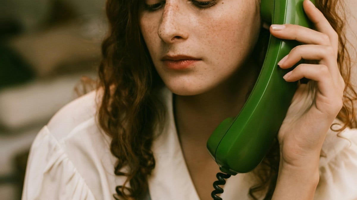 A pensive redhead woman uses a vintage green telephone, creating a nostalgic indoor scene. via Pexels