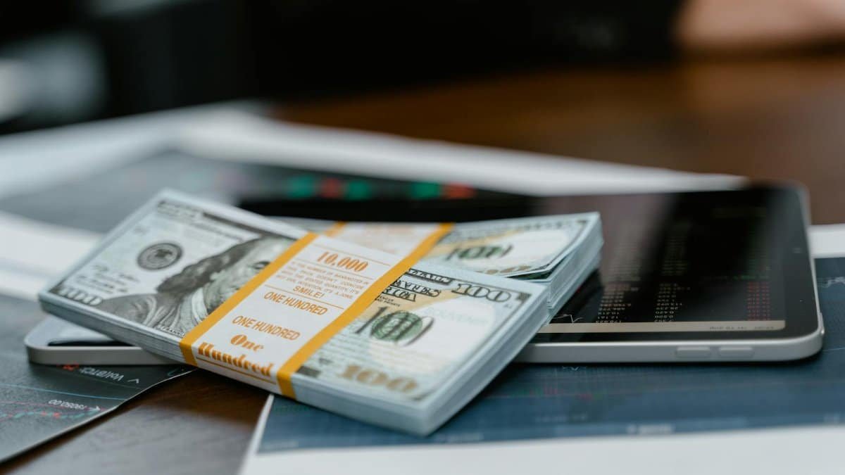 A stack of $100 bills placed on a tablet displaying financial graphs, representing modern finance.