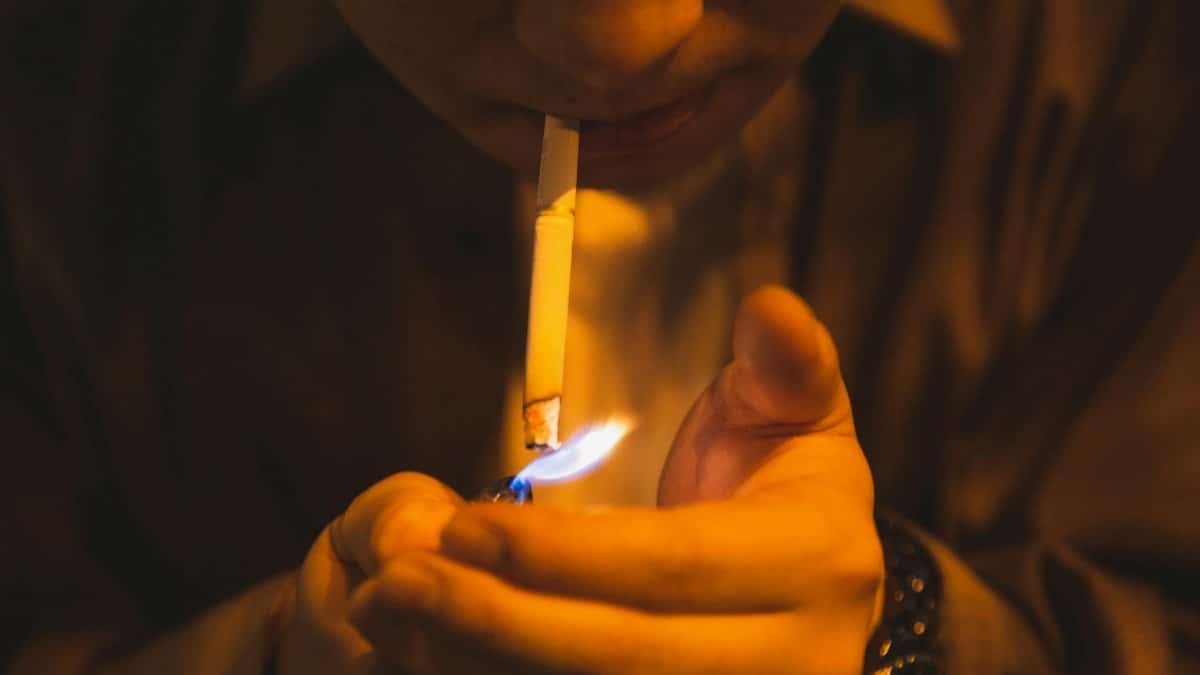 Crop male with burning lighter and cigarette smoking for reducing stress in light of lamp