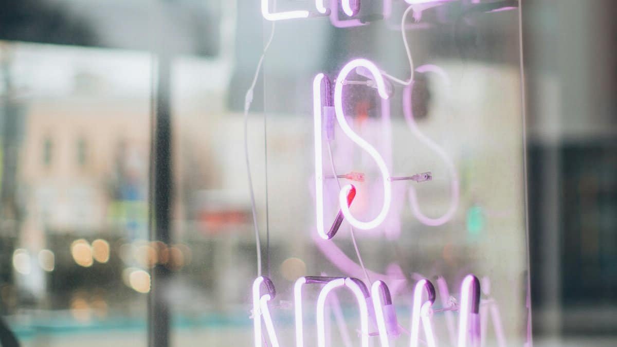 Urban scene with a glowing 'Life is Now' neon sign reflecting in a window, conveying a modern, motivational vibe.