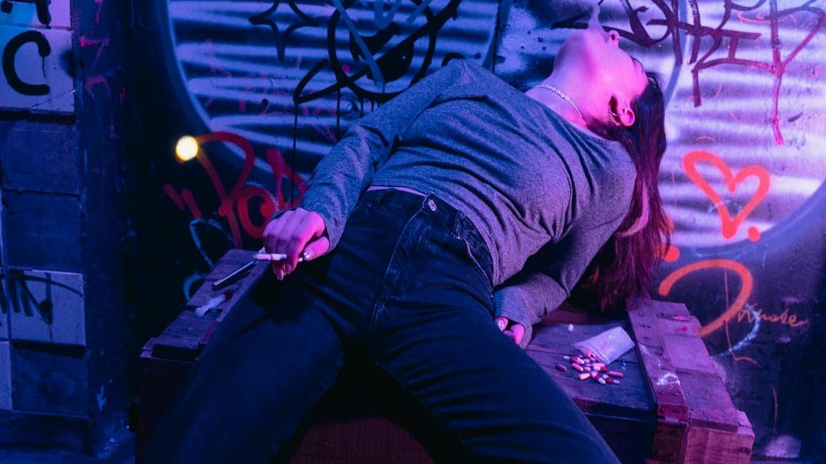 A person is reclining against a graffiti-covered wall at night.