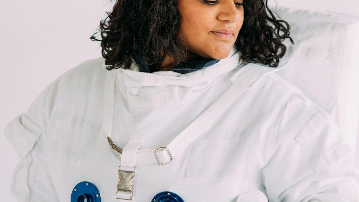 A woman wearing a detailed astronaut costume looks contemplatively to the side.