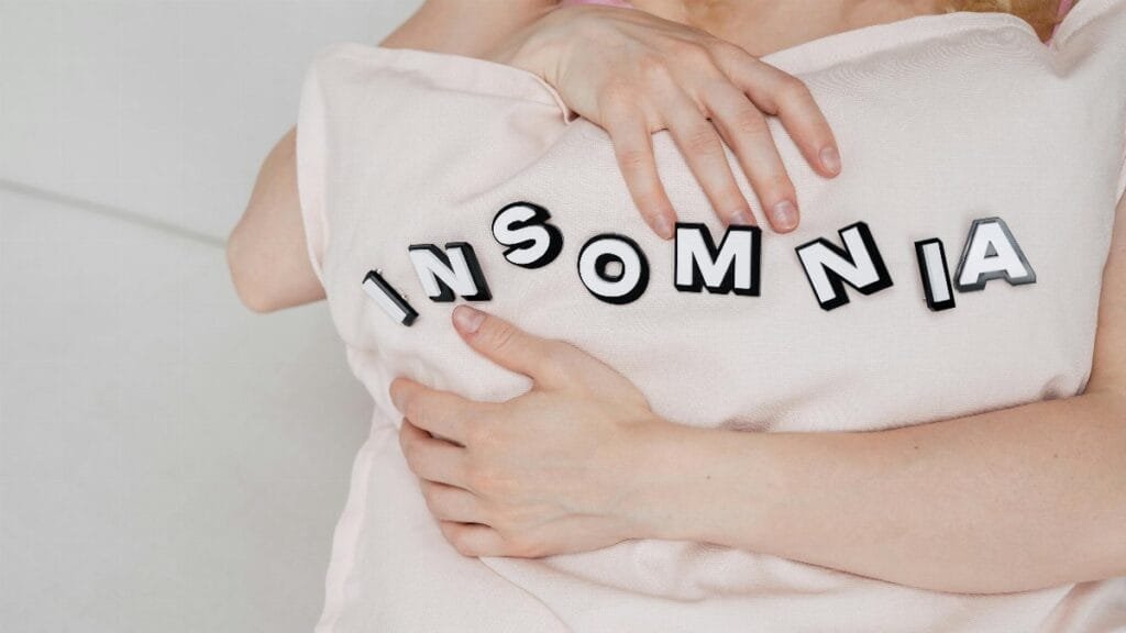 Close-up of a woman holding a pillow with 'insomnia' text, depicting sleep disorder. via Pexels