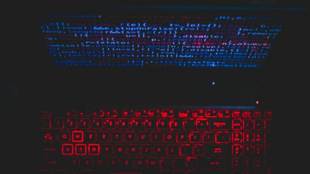 Dark-themed laptop setup with a red glowing keyboard and code on screen, ideal for tech enthusiasts.