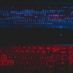 Dark-themed laptop setup with a red glowing keyboard and code on screen, ideal for tech enthusiasts.