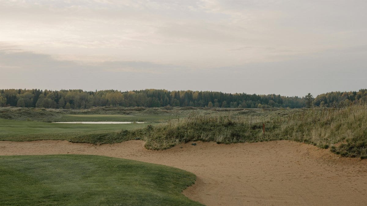 Peaceful landscape of a golf course with sand trap and distant forest at dawn.