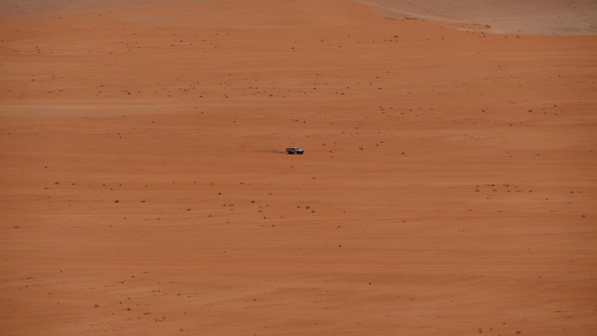 A lone vehicle traverses the vast sandy expanse of the Jordan desert, depicting isolation and adventure.