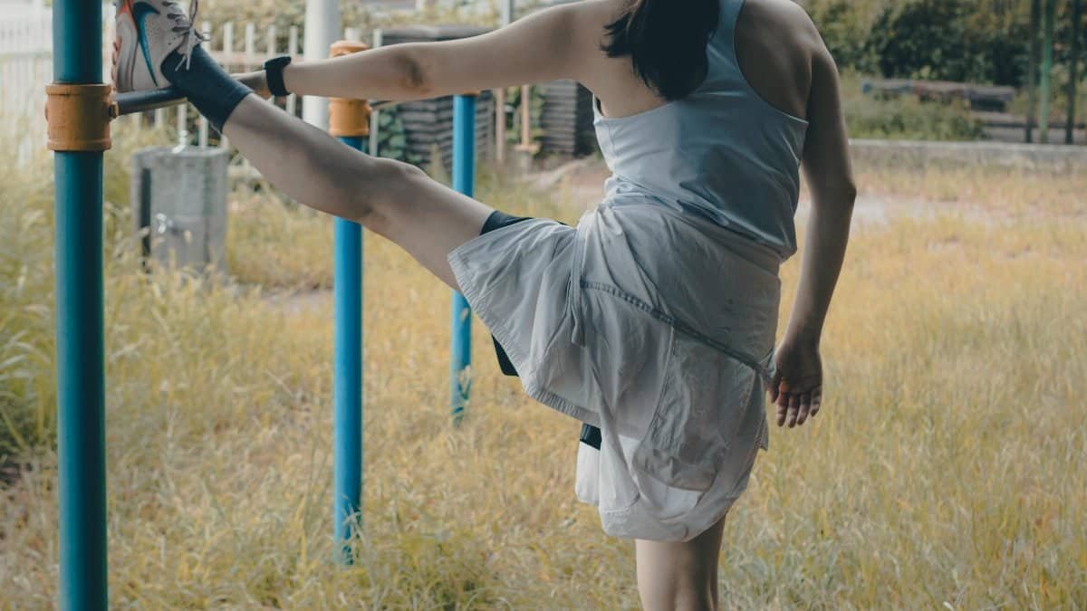 Woman stretching on a bar in a city park, showcasing fitness and wellness outdoors. via Pexels