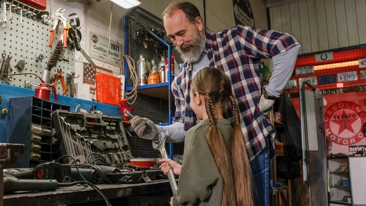 A father and daughter bonding over tools in an auto repair workshop, in a warm family moment.