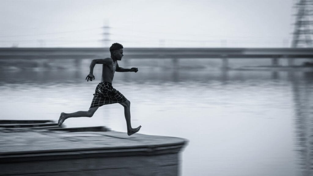 A young man in mid-air leaping over water, capturing the essence of freedom and dynamic movement. via Pexels