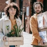 Young couple happily moving into their urban apartment with boxes and plants in daylight. via Pexels