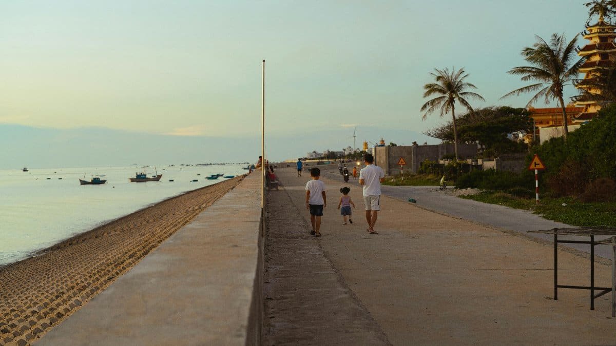 A peaceful walk along the beach in Bình Thuận, Vietnam with boats and palm trees in the background.