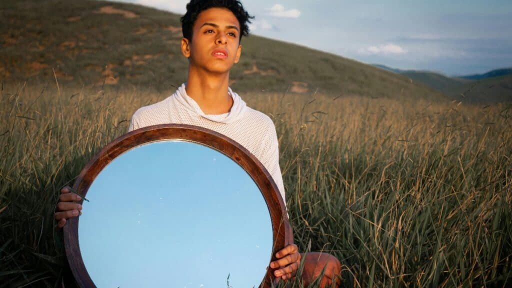 Young man in a field holding a mirror reflecting blue sky. Captured in Porto Real, Brazil. via Pexels