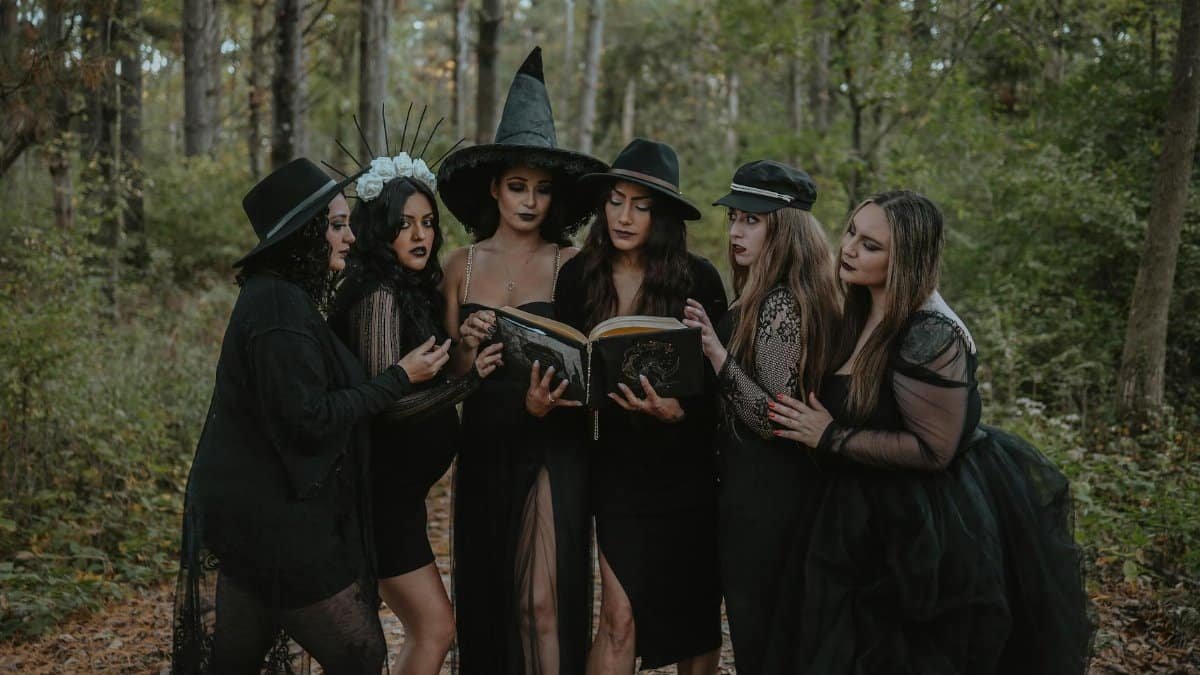 A group of women in witch costumes reading a spell book amidst an enchanting forest.