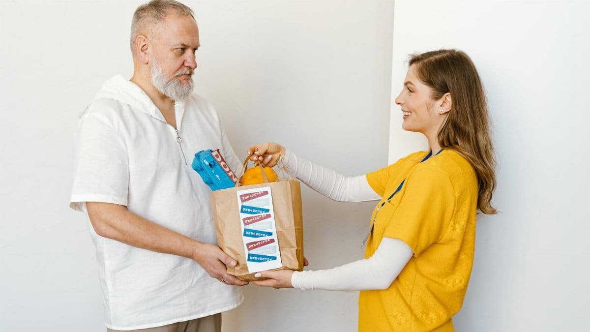 Elderly man receives donation package from smiling volunteer indoors.