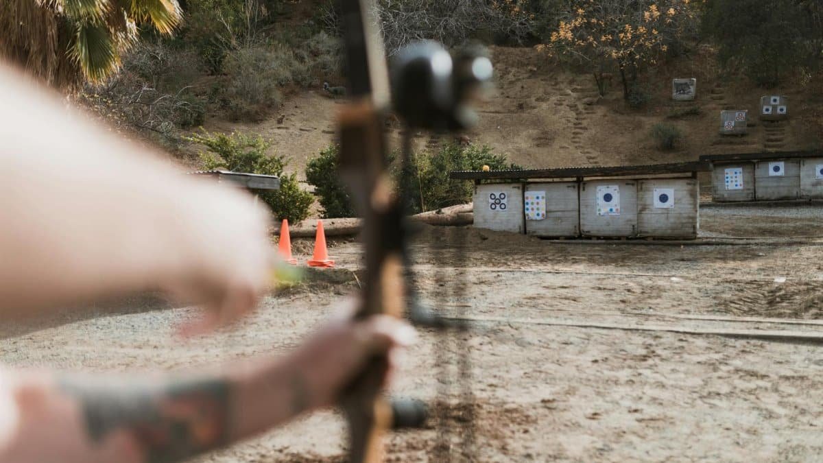 An archer aims at targets at an outdoor archery range, featuring a natural backdrop.