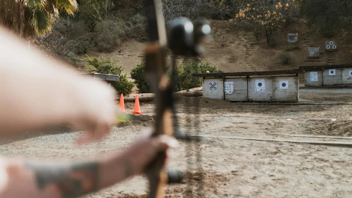 An archer aims at targets at an outdoor archery range, featuring a natural backdrop.