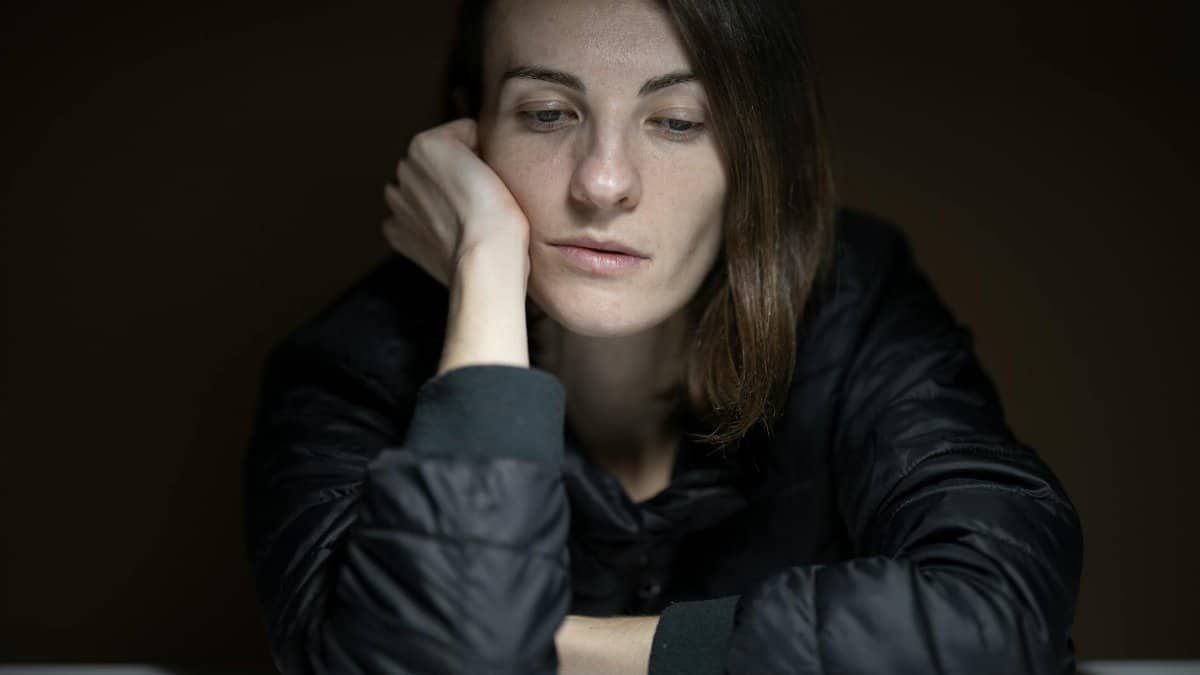 A woman in thought with a serious expression, indoors, in a low-light setting.