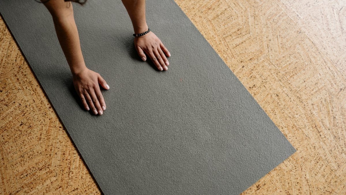 Close-up of hands on a grey yoga mat on a wooden floor, from above.