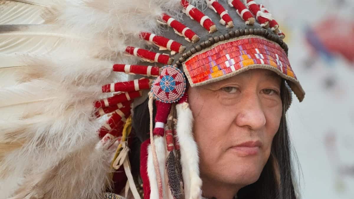 Close-up portrait of a Native American man wearing a traditional feathered headdress.