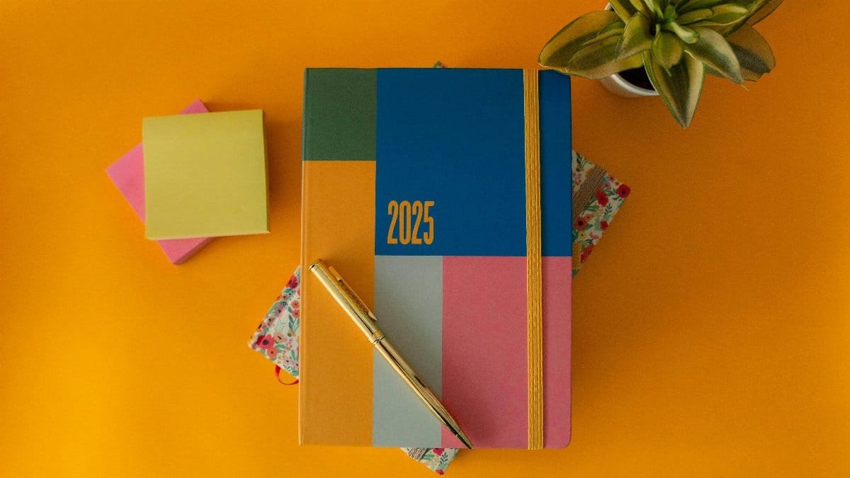 Flat lay of a vibrant 2025 planner with a pen and green plant on yellow background.