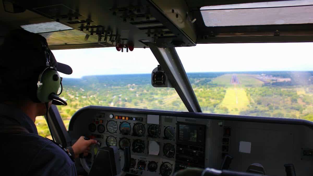 A pilot navigates the aircraft during landing approach with scenic landscape visible outside the cockpit.