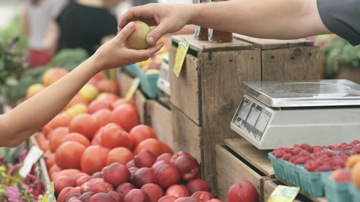 A customer exchanges an apple with a vendor at a vibrant farmers market.