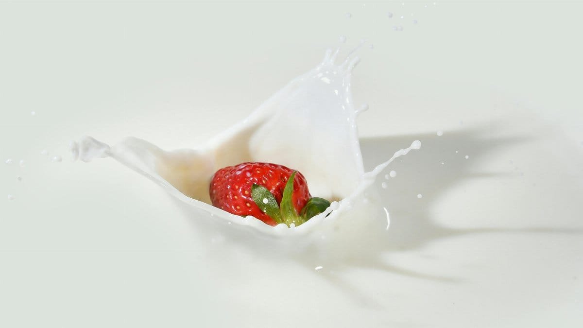 A vibrant strawberry makes a splash in creamy white milk, showcasing freshness and vivid colors.