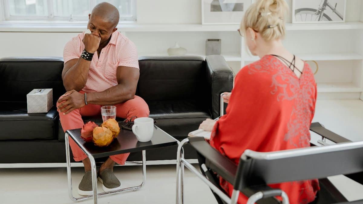A man expresses emotions during a therapy session with a therapist in a modern office setting. via Pexels