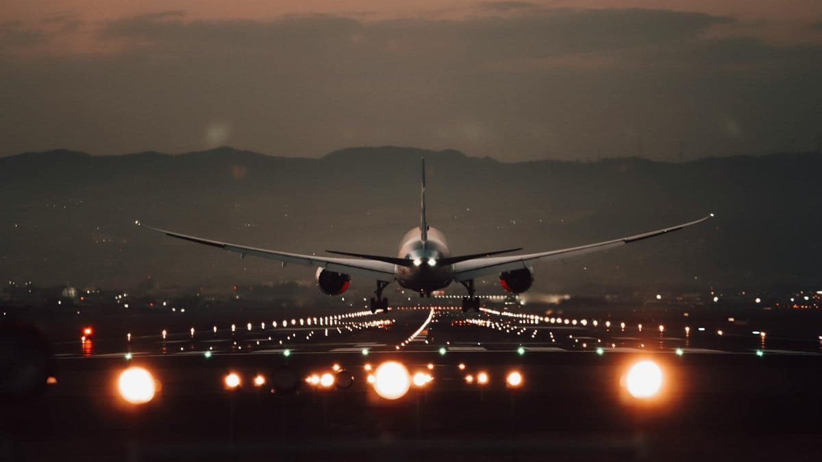 A large airplane makes a dramatic landing on a lit runway at twilight with a scenic mountain backdrop.
